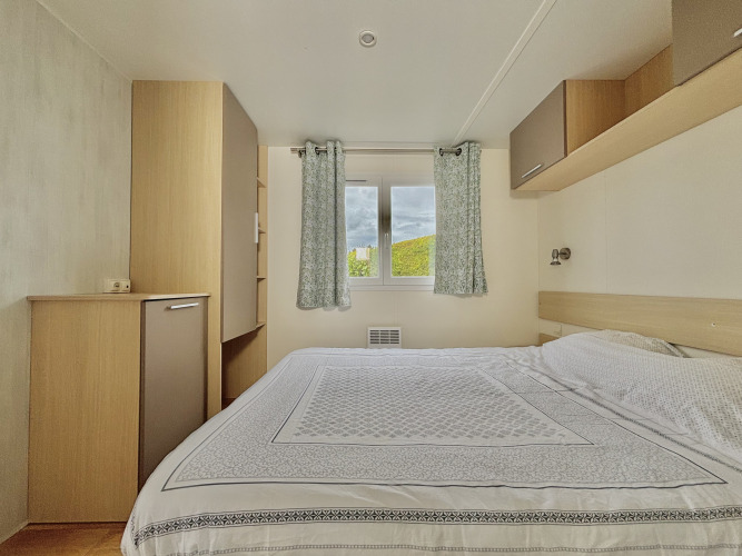 Dormitorio con cama doble, cortinas claras y vista a la naturaleza en Cottage Zen, Camping Seasonova Le Point du Jour.