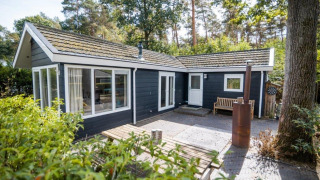 Buitenaanzicht van Nature Chalet in een bosrijke omgeving, met terras, bankje en moderne decoratie.
