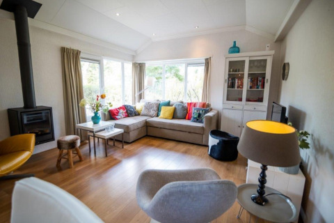Modern living room at Nature Chalet, Bospark Markelo, Netherlands, with corner sofa, fireplace and windows.