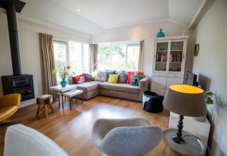 Moderne woonkamer in het Nature Chalet in Bospark Markelo, Nederland, met hoekzetel, haard en ramen.