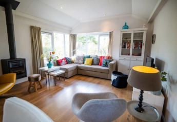 Moderne woonkamer in het Nature Chalet in Bospark Markelo, Nederland, met hoekzetel, haard en ramen.