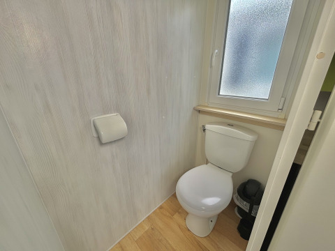 Lyst og lille badeværelse med toilet, toiletpapirholder og vindue i Cottage Zen, Camping Seasonova Le Point du Jour.
