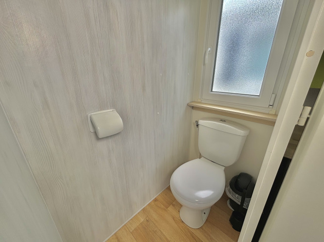 Pequeño y luminoso baño con inodoro, portapapel higiénico y ventana en Cottage Zen, Camping Seasonova Le Point du Jour.