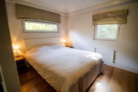 Dormitorio con cama doble, mesitas y ventanas en Nature Chalet, Bospark Markelo, Países Bajos.