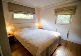 Dormitorio con cama doble, mesitas y ventanas en Nature Chalet, Bospark Markelo, Países Bajos.