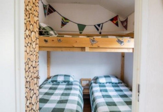 Schlafzimmer mit zwei Einzelbetten, Hochbett und karierten Bettdecken im Nature Chalet in Bospark Markelo.