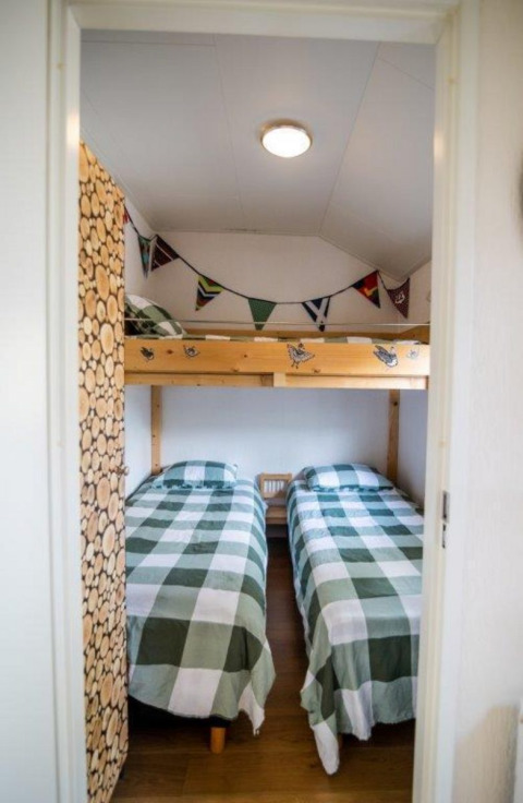 Værelse med to enkeltsenge, køjeseng øverst og ternet sengetøj i et chalet i Bospark Markelo, Holland.