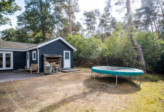 Vue du Nature Chalet à Bospark Markelo, Pays-Bas, avec trampoline et forêt environnante verdoyante.