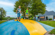Des enfants s'amusent sur un grand coussin gonflable dans un parc de vacances glamping, des adultes regardent.
