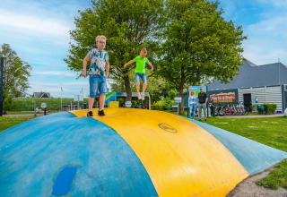 Kinder spielen auf einem großen Hüpfkissen in einem Ferienpark mit Glamping, während Erwachsene zusehen.
