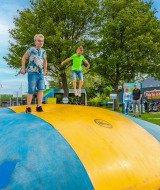 Niños juegan sobre una gran almohadilla inflable en un parque de vacaciones con glamping, adultos observan cerca.
