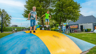 Niños juegan sobre una gran almohadilla inflable en un parque de vacaciones con glamping, adultos observan cerca.