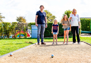 Gezin speelt petanque op een zonnig pleintje in een vakantiepark met glamping accommodaties.