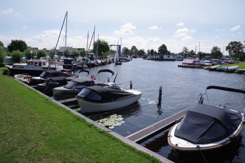 Photo of a harbor with boats at a holiday park, showing glamping accommodations and green grassy areas.