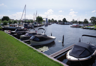 Havenzicht met boten aan een vakantiedomein, glamping accommodaties en groene zones langs het water.