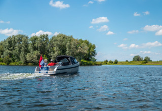 Mensen varen met een boot op een meer bij een vakantiepark met glamping, omgeven door natuur.