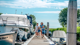 Familia caminando por un muelle entre barcos en un parque de vacaciones con glamping y buen clima.