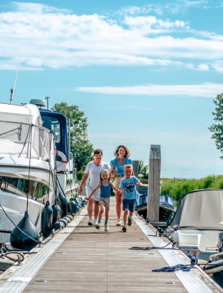 Familia caminando por un muelle entre barcos en un parque de vacaciones con glamping y buen clima.