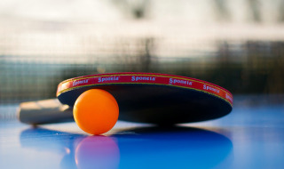 Tafeltennisbat en oranje bal op tafel, foto genomen bij een vakantiepark met glamping verblijven.