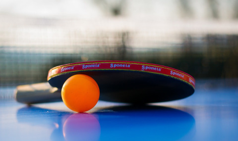 Table tennis paddle and orange ball on table, photo taken at a holiday park with glamping options.
