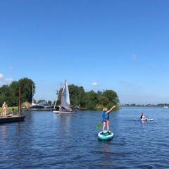 Parque vacacional con glamping; personas remando, navegando y disfrutando junto al lago soleado.