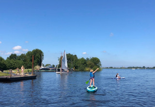 Parco vacanze con glamping: persone fanno sup, vela e si godono il lago soleggiato e la natura.