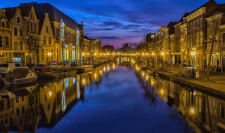 Foto nocturna de un pintoresco canal flanqueado por edificios y farolas reflejadas en el agua.
