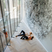 Dos personas recostadas en el suelo de un moderno parque de glamping, junto a gran arte mural y ventanas de vidrio.