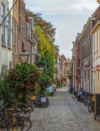 Calle adoquinada con bicicletas, flores y casas históricas, ideal para una experiencia vacacional única.