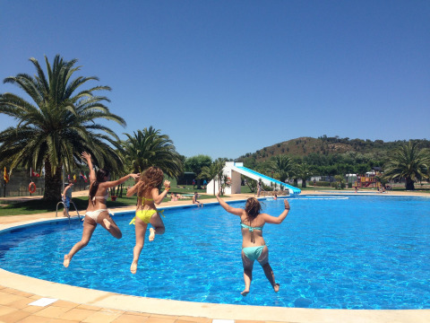Tres mujeres saltan a la piscina en Camping Mas Patoxas, un parque vacacional en Cataluña, España, día soleado.