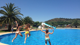 Drie vrouwen springen in het zwembad bij Camping Mas Patoxas, een vakantiepark in Catalonië, Spanje op een zonnige dag.