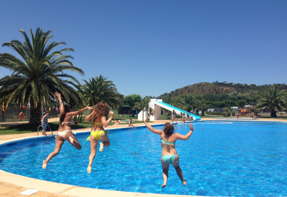 Tres mujeres saltan a la piscina en Camping Mas Patoxas, un parque vacacional en Cataluña, España, día soleado.