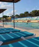 Piscina en Camping Mas Patoxas en Cataluña con tumbonas azules, toldos y gente disfrutando el verano.
