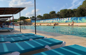Piscine du Camping Mas Patoxas en Catalogne avec transats bleus, parasols et vacanciers baignants.
