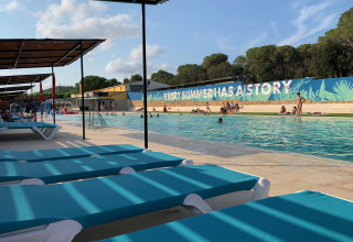 Piscina en Camping Mas Patoxas en Cataluña con tumbonas azules, toldos y gente disfrutando el verano.