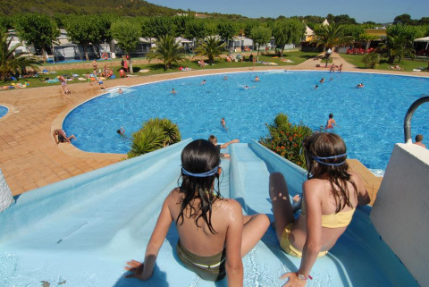 Bambini su uno scivolo d'acqua accanto a una grande piscina al Camping Mas Patoxas, villaggio vacanze in Catalogna, Spagna.