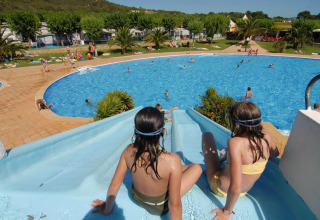 Bambini su uno scivolo d'acqua accanto a una grande piscina al Camping Mas Patoxas, villaggio vacanze in Catalogna, Spagna.