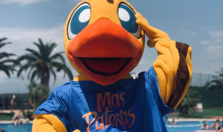 Mascota con disfraz de pato del Camping Resort Mas Patoxas junto a la piscina con bañistas de fondo.