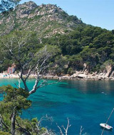 Vista de una pintoresca cala cerca de Pals, Cataluña, con aguas turquesas, barcos y colinas verdes al fondo.