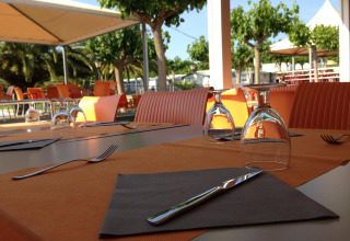 Area pranzo all’aperto con sedie arancioni al Camping Mas Patoxas, villaggio vacanze in Catalogna, Spagna.