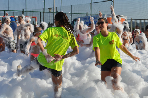 People enjoying a foam party outdoors at Camping Mas Patoxas holiday park in Catalonia, Spain, wearing bright shirts.