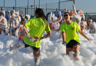 Persone che si divertono a una festa di schiuma all'aperto al Camping Mas Patoxas in Catalogna, Spagna, con magliette colorate.