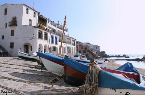 Fishing boats on the sandy shore in front of whitewashed buildings in the coastal town of Pals, Catalonia, Spain.