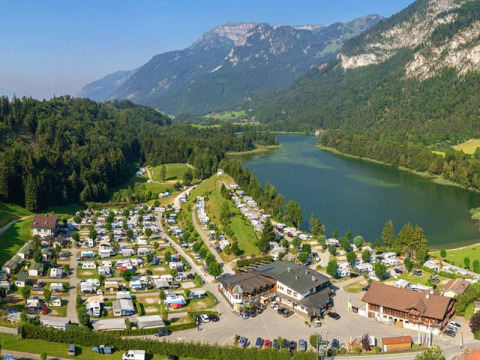 Camping Seeblick Toni en Tirol, Austria con caravanas, lago pintoresco y montañas verdes de fondo.