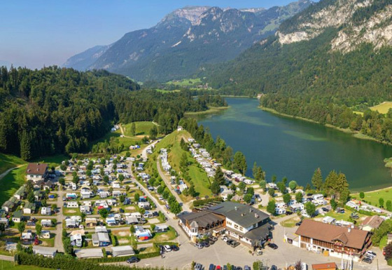 Campingpladsen Seeblick Toni i Tirol, Østrig, med søudsigt, bjerge og mange campingvogne og telte.