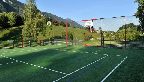 Cancha deportiva con aro de baloncesto y red en Camping Seeblick Toni, Tirol, Austria, rodeada de naturaleza.