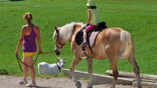 Un niño monta a caballo guiado por un adulto en Camping Seeblick Toni, un parque vacacional en Tirol, Austria.