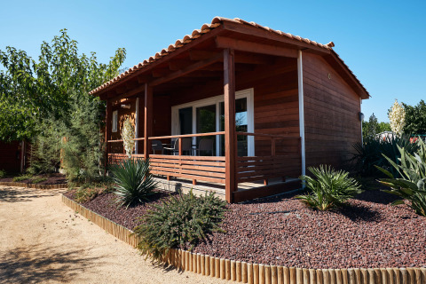 Houten chalet Bungalow Quermany met overdekte veranda en woestijntuin onder een heldere blauwe lucht.