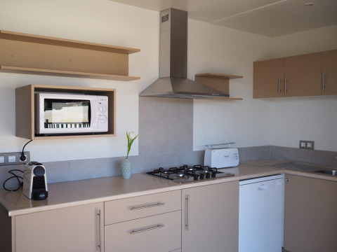 Moderne keuken in Bungalow Quermany op Camping Mas Patoxas, Spanje, met fornuis, magnetron en koffiemachine.