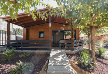 Wooden chalet Bungalow Quermany with a covered porch, surrounded by trees and landscaped garden plants.